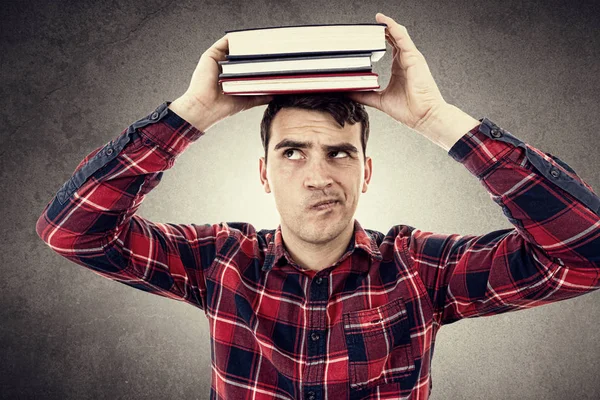 Thinking Young man student holding a  stack of books on head