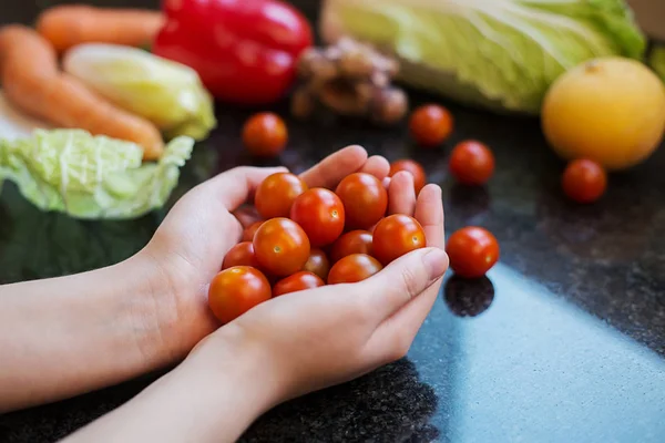 Woman holding cherry tomatoes in hands home with vegetables in background