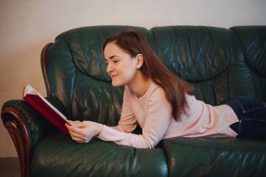 Holding ve ev kanepede yatan kitap okuma öğrenci kız