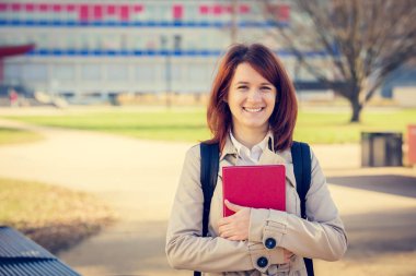 Açık havada bir kırmızı kitap tutan genç gülümseyen öğrenci profesyonel