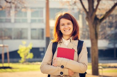 Genç öğrenci kız bir kitap Üniversitesi arka plan üzerinde gülümseyen .