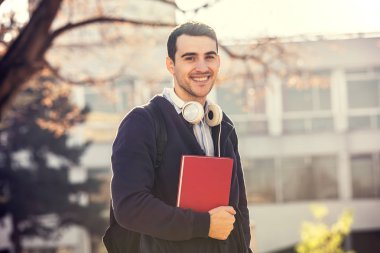 Bir kitap ve bir çanta Üniversitesi arka plan üzerinde tutan University.Smiling genç öğrenci adam 