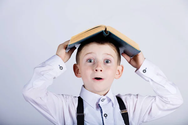 Surpreendido, bonito pequeno schoo boyl com um livro aberto em sua cabeça — Fotografia de Stock