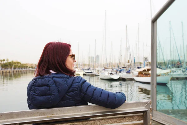 Młode ładne turystycznego kobieta siedzi na drewnianym molo, w pobliżu morza i patrząc na miasto — Zdjęcie stockowe