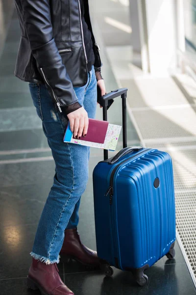 Young Woman with Traveling luggage in airport terminal with passport and a tourist map