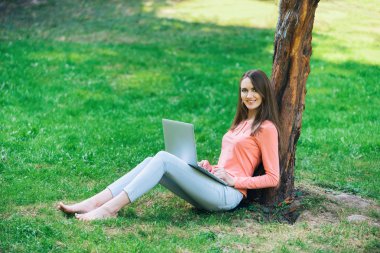 Yeşil bir parkta dizüstü bilgisayarla çalışan öğrenci kız.