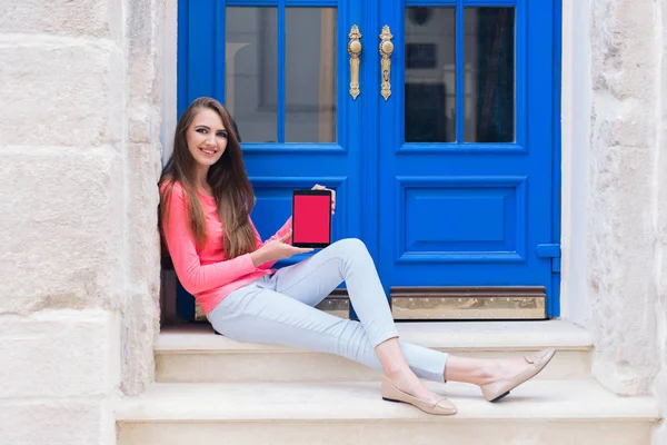 Mavi kapı önünde bir tablet ile oturan öğrenci kız