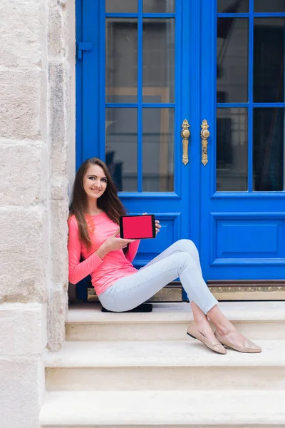 Mavi kapı önünde bir tablet ile oturan öğrenci kız