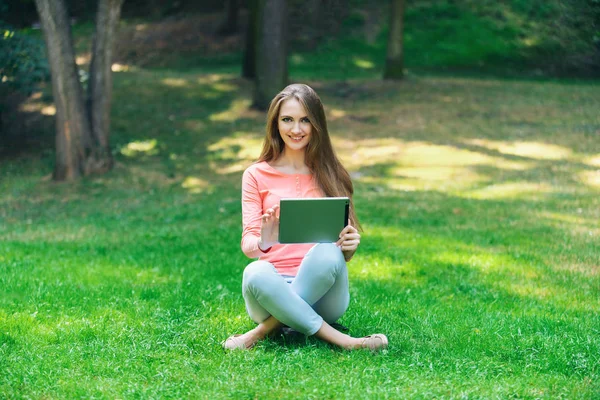 Student tjej arbetar med en platta i en grönskande park — Stockfoto
