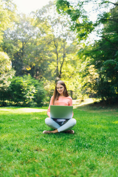 Student girl working with a laptop in a green park