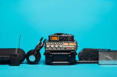 mavi arka plan üzerinde kayıt alan ses donatımı. Ön cam, shotgun mikrofon, radyo sistemi, boompole, yazmak, taşınabilir durumda, mikser ve kulaklıklar