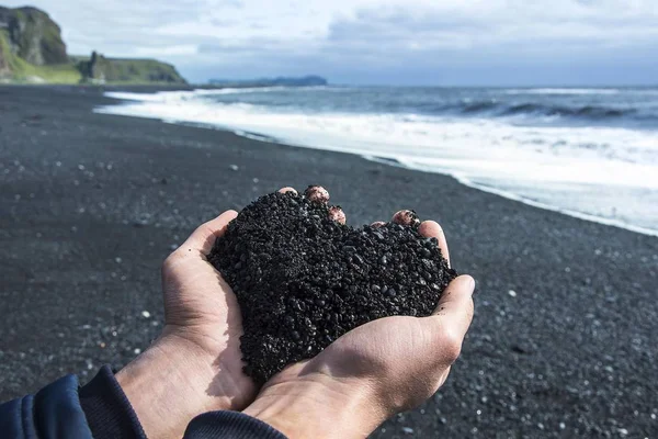 Icelandic black sand held in a man\'s hands, resembling a heart