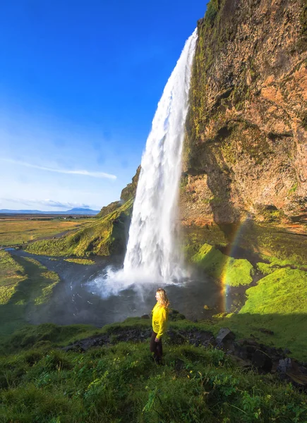 Γυναίκα κάτω από Seljalandsfoss καταρράκτη, Ισλανδία. Ηλιόλουστη μέρα στην Ισλανδία με ουράνιο τόξο — Φωτογραφία Αρχείου