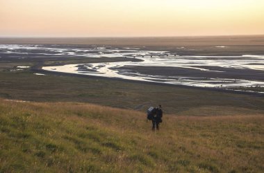 Seljalandsfoss, İzlanda Nehri Vadisi üzerinde güneşin tadını bir dağ kenarında yürüyen adam. Mercek parlaması ile.