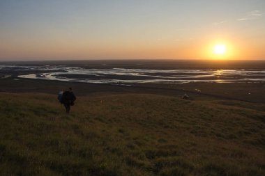 Seljalandsfoss, İzlanda Nehri Vadisi üzerinde güneşin tadını bir dağ kenarında yürüyen adam. Mercek parlaması ile.