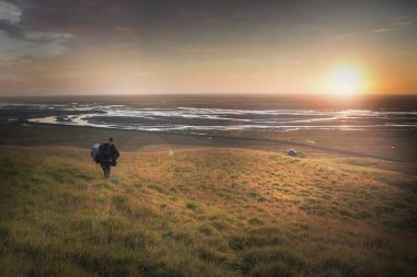 Seljalandsfoss, İzlanda Nehri Vadisi üzerinde güneşin tadını bir dağ kenarında yürüyen adam. Mercek parlaması ile.