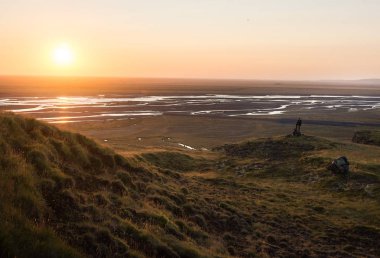 Seljalandsfoss, İzlanda Nehri Vadisi üzerinde güneşin tadını bir dağ kenarında yürüyen adam. Mercek parlaması ile.