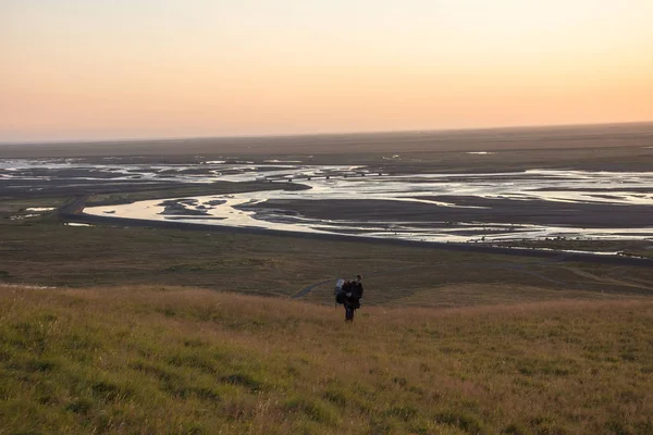 Seljalandsfoss, İzlanda Nehri Vadisi üzerinde güneşin tadını bir dağ kenarında yürüyen adam. Mercek parlaması ile.