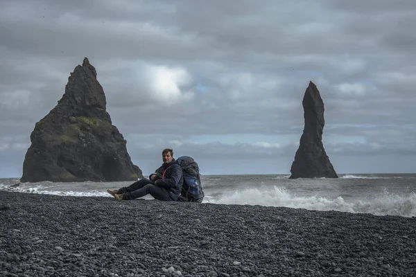 Turista con mochila sentada en la playa de arena negra, Vik en Islandia — Foto de Stock