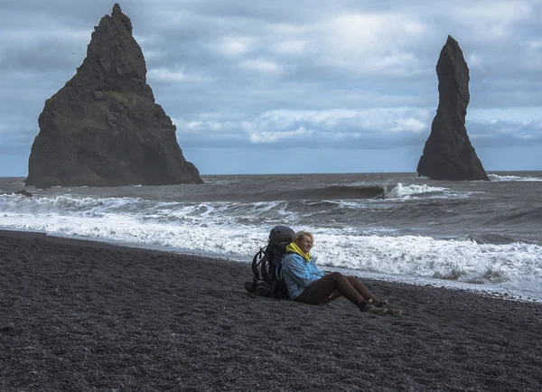 Turista con mochila sentada en la playa de arena negra, Vik en Islandia — Foto de Stock
