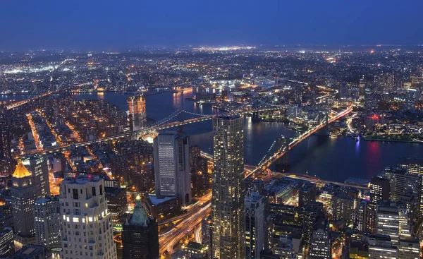 El puente de Brooklyn y el horizonte de Manhattan de la ciudad de Nueva York iluminados por la noche con una luna llena por encima . — Foto de Stock