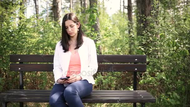 Atrakcyjne uśmiechający się młoda kobieta z smartphone w parku. Przesuń suwak — Wideo stockowe