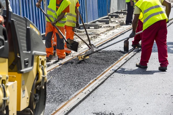 Workers construct asphalt road and railroad lines — Stock Photo, Image