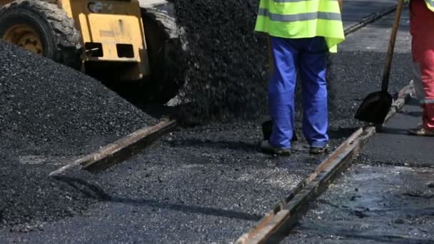 労働者のチームは 路面電車の沿線の街に熱いアスファルトを置きます 道路工事の労働者保護の制服でシャベルで ショベル バガーと暑い日で働く — ストック動画