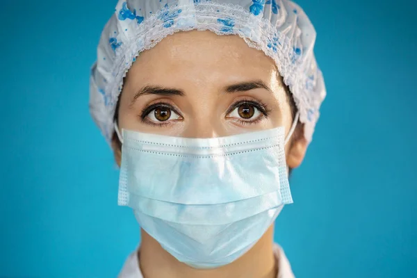在Covid 19爆发流行病期间 有蓝色防护帽和外科口罩的护士 近景肖像画与单一使用蓝色保护面具在脸上 Studio 免版税图库照片