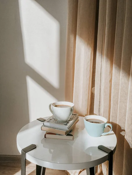 Warm cozy home. Couple cups of coffee with book on a white table . Sunshine appartment