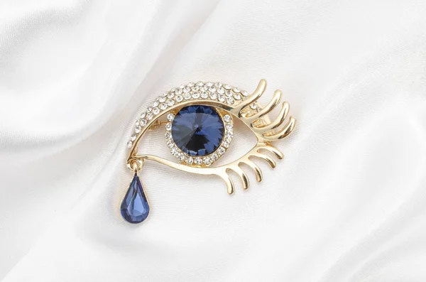 Olho de broche de ouro com diamantes com safira grande em um tecido de seda — Fotografia de Stock