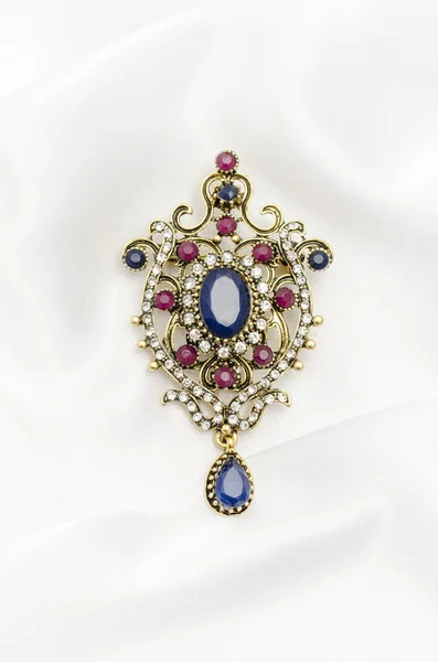 Vintage gold brooch with precious stones on white silk — Stock Photo, Image