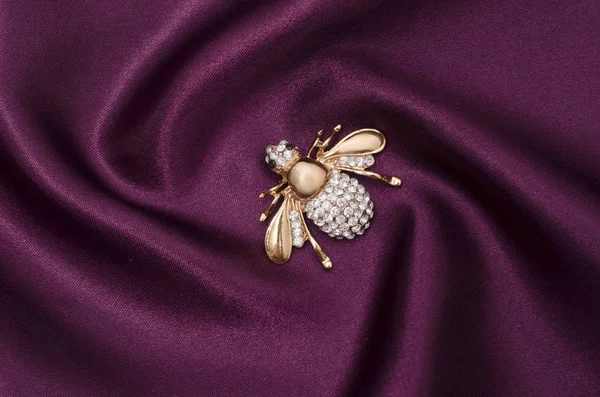 Broche de abeja dorada con diamantes en tela de seda —  Fotos de Stock