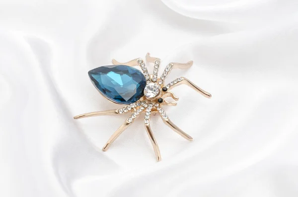 Goldene Spinne mit einem großen blauen Stein auf Seidenstoff — Stockfoto