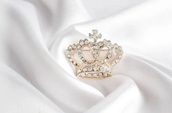 Golden brooch crown isolated on white silk — Stock Photo, Image
