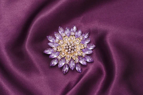 Round purple brooch with diamonds on silk fabric
