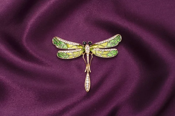 Эмалевая брошь с золотой стрекозой с бриллиантами на шелковой ткани — стоковое фото