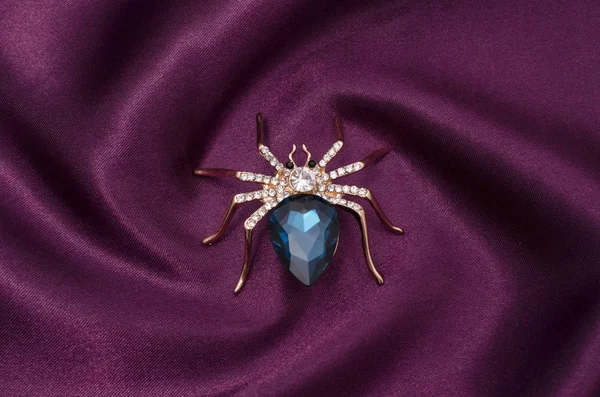 Золотой паук с большим синим камнем на шелковой ткани — стоковое фото
