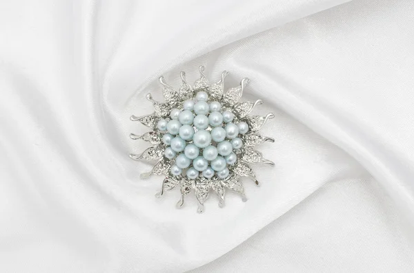 Круглая серебряная брошь с голубым жемчугом на шелковой ткани — стоковое фото