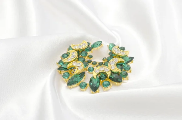 Broche dorado con esmeraldas y diamantes sobre seda —  Fotos de Stock