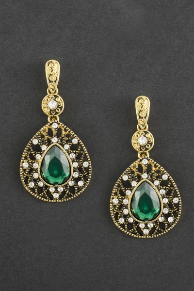 gold drop earrings with green stone isolated on black