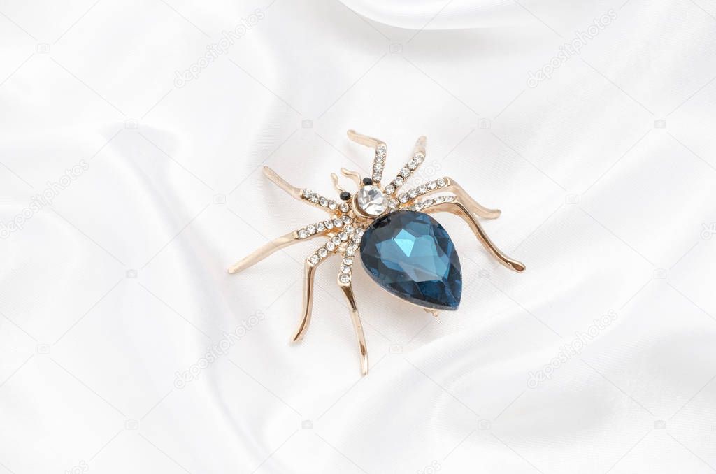 Golden spider with a big blue stone on silk fabric