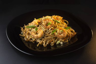 Makarna, karides ve siyah tabakta otlar.