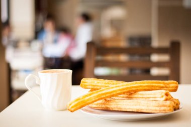 Küçük tabakta birkaç churro ve çikolatalı süt.