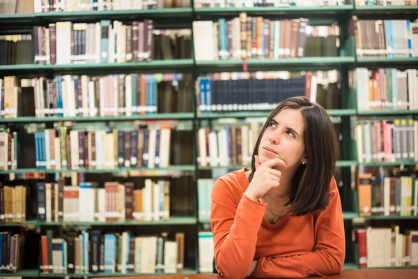 В библиотеке - симпатичная студентка, думающая, работающая в библиотеке. — стоковое фото