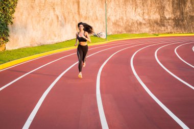 Genç bayan koşucu atletizm pistinde koşuyor.