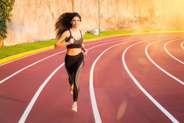 Genç bayan koşucu atletizm pistinde koşuyor.