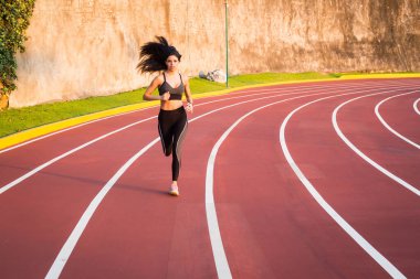 Genç bayan koşucu atletizm pistinde koşuyor.