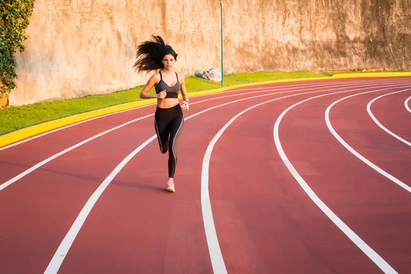 Genç bayan koşucu atletizm pistinde koşuyor.