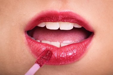 Cosmetics, makeup and skin care concept. Close up of woman applying lipstick or lip gloss to her plump pink lips. clipart